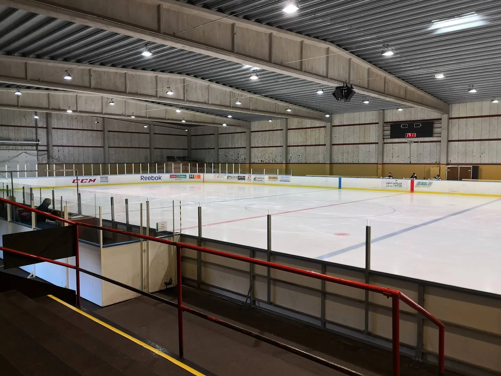 Empty ice at Österås ishall in Hässleholm seen from the stands, with the boards and the scoreboard under the steel-beam roof — Österås ishall