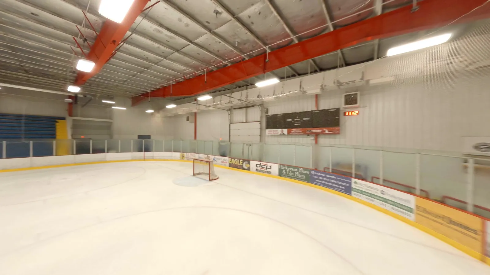 The ice at the Otsego County Sportsplex from rink level, with the net, the boards and the orange roof steel — Otsego County Sportsplex