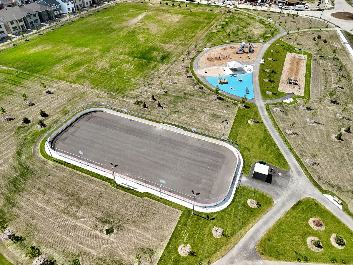 Aerial view of Babe McRae Park, with the boarded rink pad, the playground, the splash pad and a small service building. — Babe McRae Park Outdoor Rink