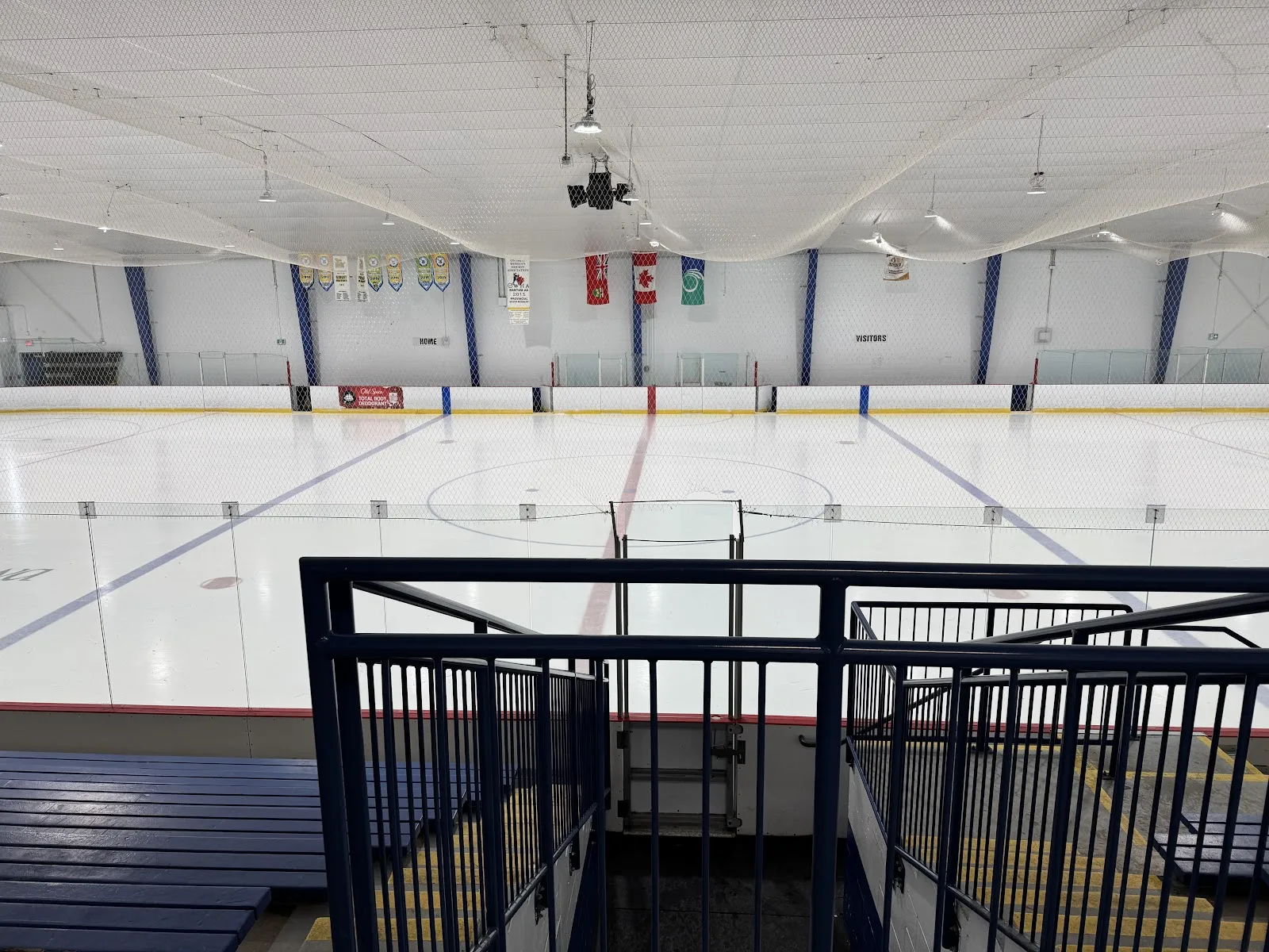 El hielo vacío de Bell Centennial Arena visto desde las gradas azules, con banderas y mantas colgando en el extremo lejano. — Bell Centennial Arena