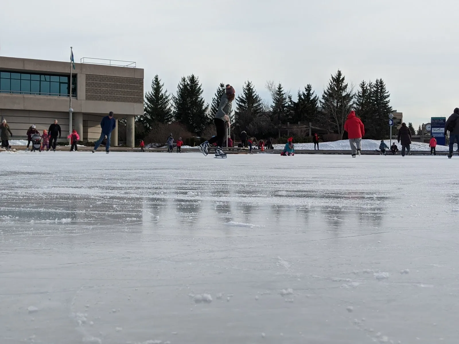 The flooded Ben Franklin Place rink in winter, a wide pale sheet of ice with a snow bank around it and the glass and stone civic centre across the park. — Ben Franklin Place Outdoor Rink
