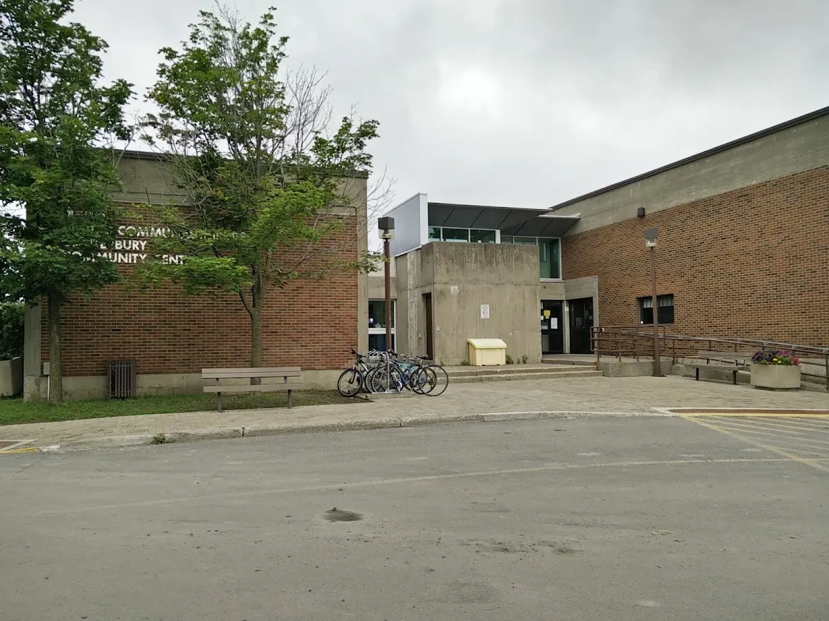 Patio de entrada del edificio del Canterbury Community Centre, de ladrillo con un letrero parcial de 'Canterbury Community Centre' en la pared, una banca y un bicicletero junto a las puertas. — Canterbury Recreation Complex – Brian Kilrea Arena