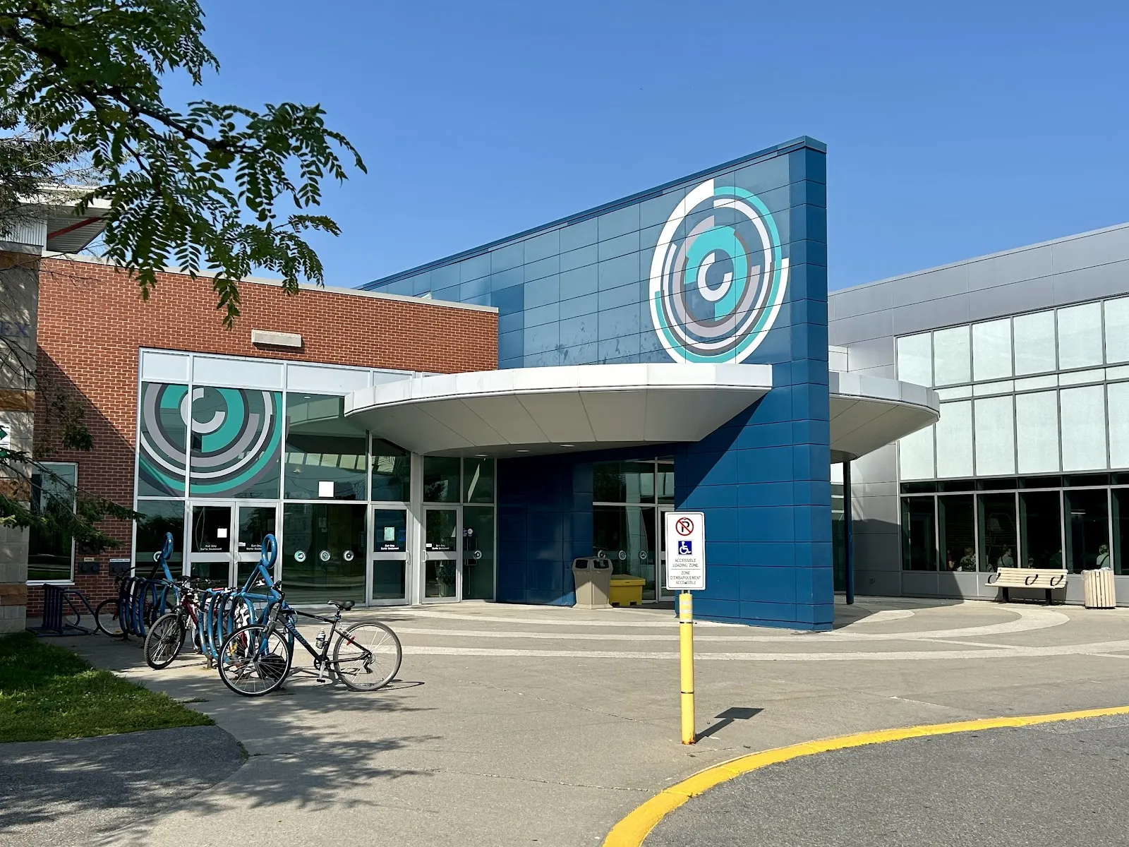 The blue and brick entrance of the CARDELREC Recreation Complex in Stittsville with its circular logo above the curved canopy and bicycles at the racks — CARDELREC Recreation Complex Goulbourn