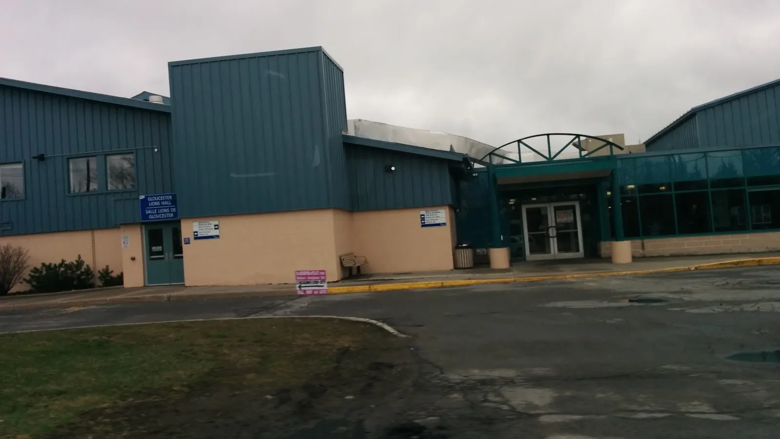 La fachada de la Fred Barrett Arena en Leitrim Road, en Ottawa, con revestimiento verde azulado y una entrada de vidrio en arco, en un día gris — Fred Barrett Arena