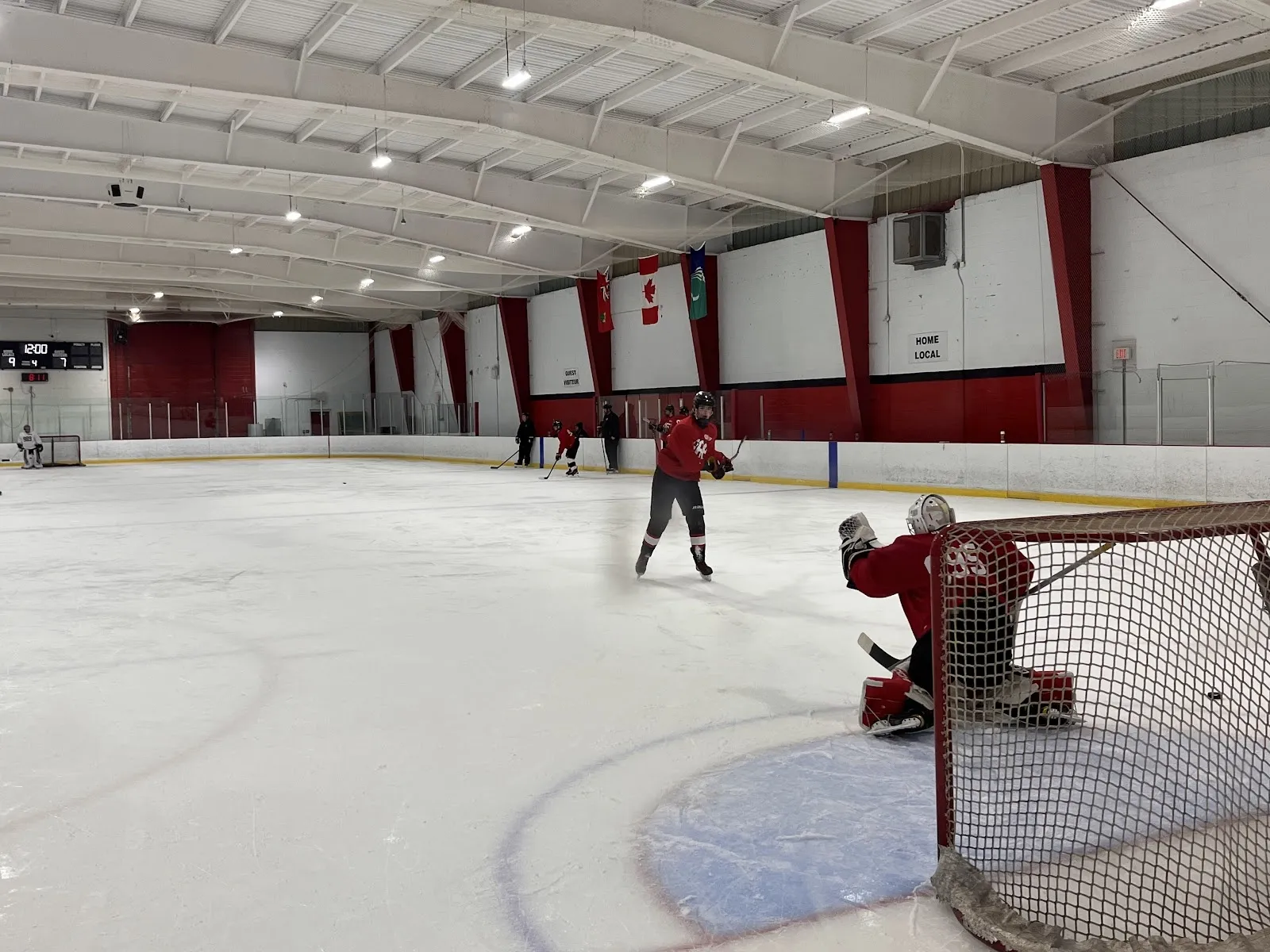 Una vista amplia a lo largo de la pista con un portero en la portería en primer plano y paredes con paneles rojos y blancos en el lado opuesto. — Howard Darwin Centennial Arena
