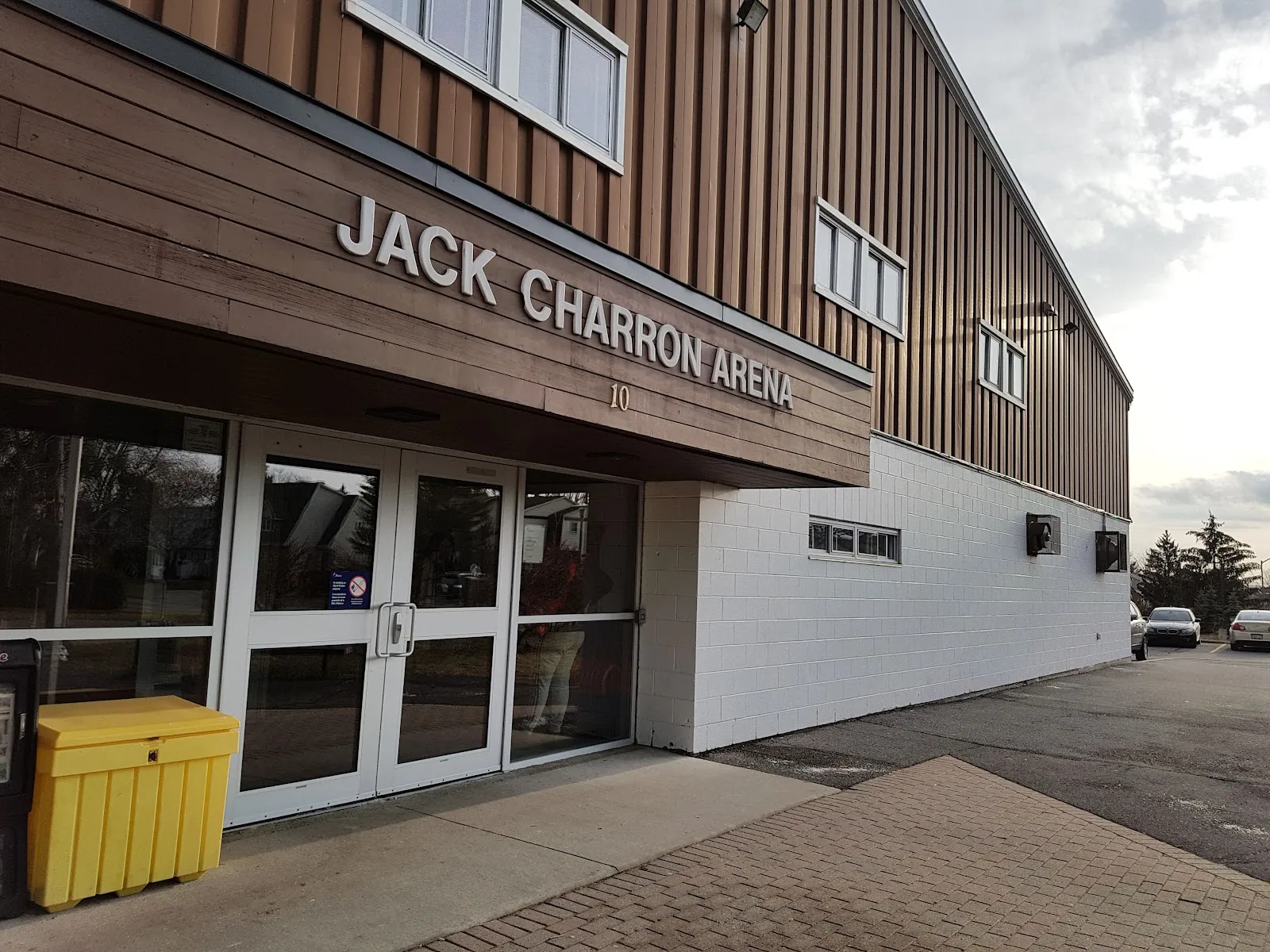 The entrance of the Jack Charron Arena in Kanata with its name in metal letters on the wood-clad canopy above the glass doors — Jack Charron Arena