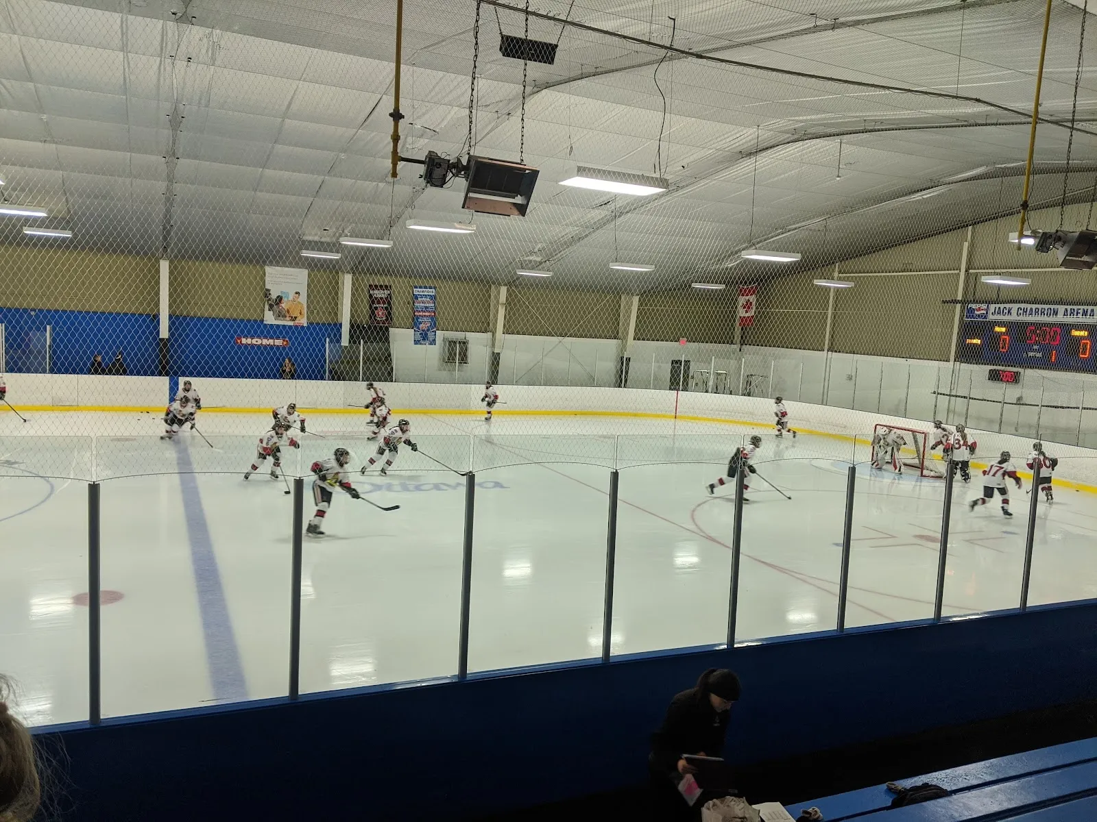 A public session spread across a wide sheet seen over the glass, blue boards and a steel-framed roof with a long wall behind. — Jack Charron Arena