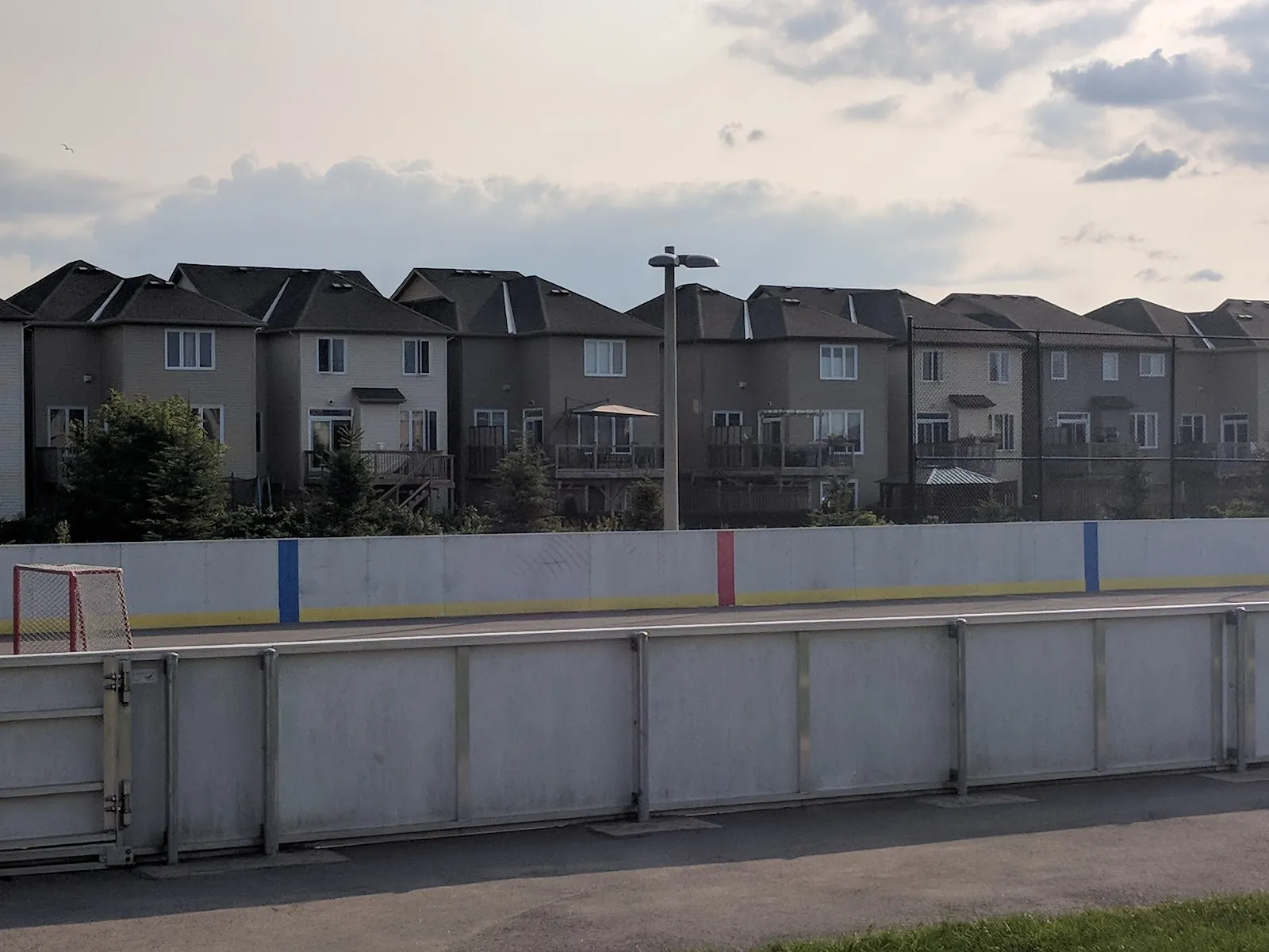 The boarded rink at Kristina Kiss Park in summer, white boards with red and blue trim in front of townhouses. — Kristina Kiss Park Outdoor Rink