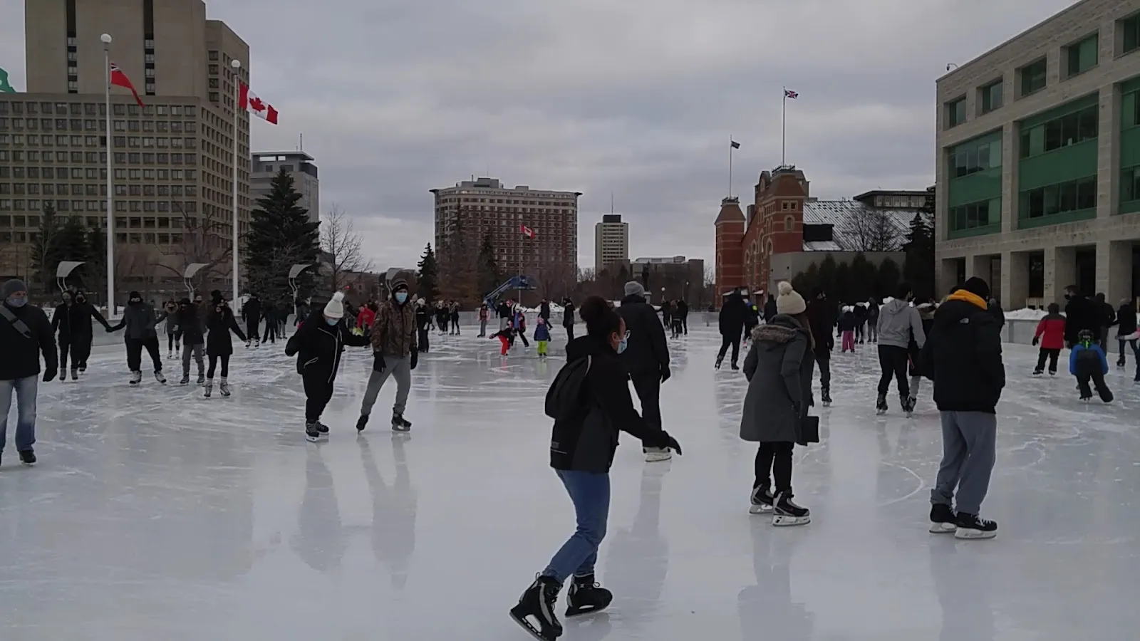 The Marion Dewar Plaza rink in front of Ottawa City Hall, skaters spread across the lit ice with the glass and stone towers of downtown beyond. — Marion Dewar Plaza (Rink of Dreams) Outdoor Rink