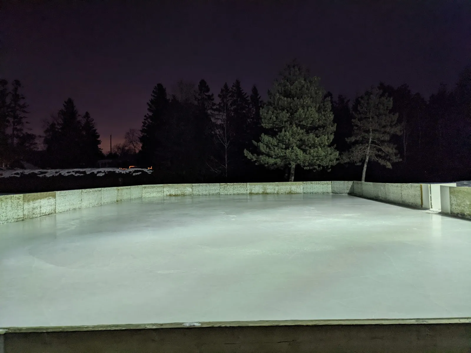 The empty boarded outdoor rink at Mary Durling Park in Stittsville at dusk, with its pale boards and the dark pines behind — Mary Durling Park Outdoor Rink