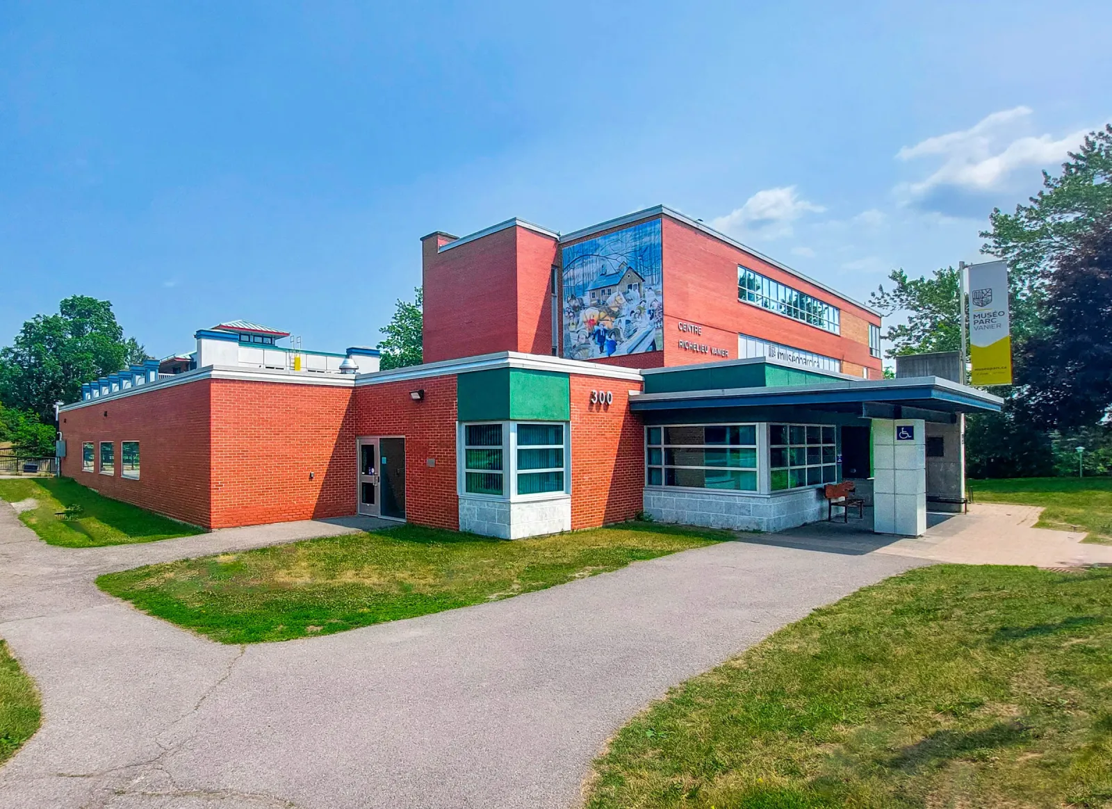 The red-brick building at 300 Pères-Blancs Avenue in Richelieu-Vanier Park, with a large mural on its upper wall and a path across the lawn to the entrance. — Richelieu Park Outdoor Rink