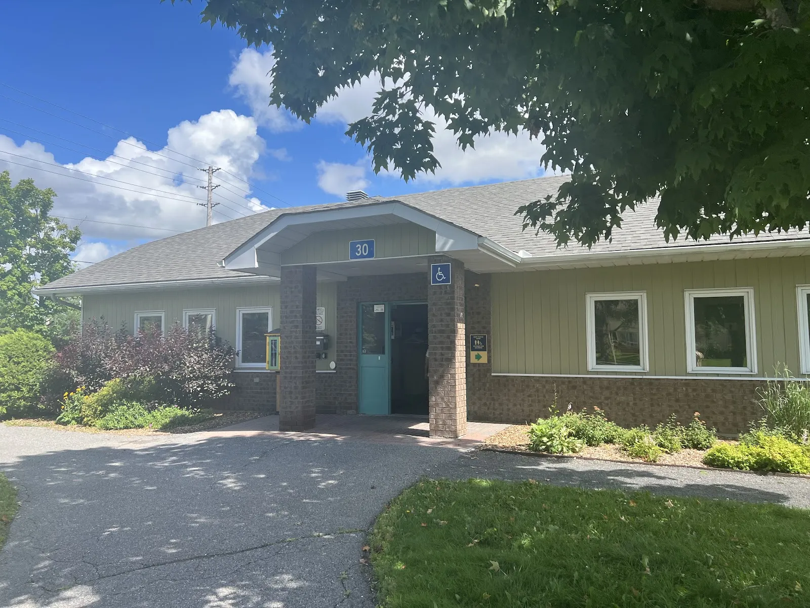 La casa club de Tanglewood Park, un edificio bajo color beige con entrada techada al final de un sendero pavimentado. — Tanglewood Park Outdoor Rink