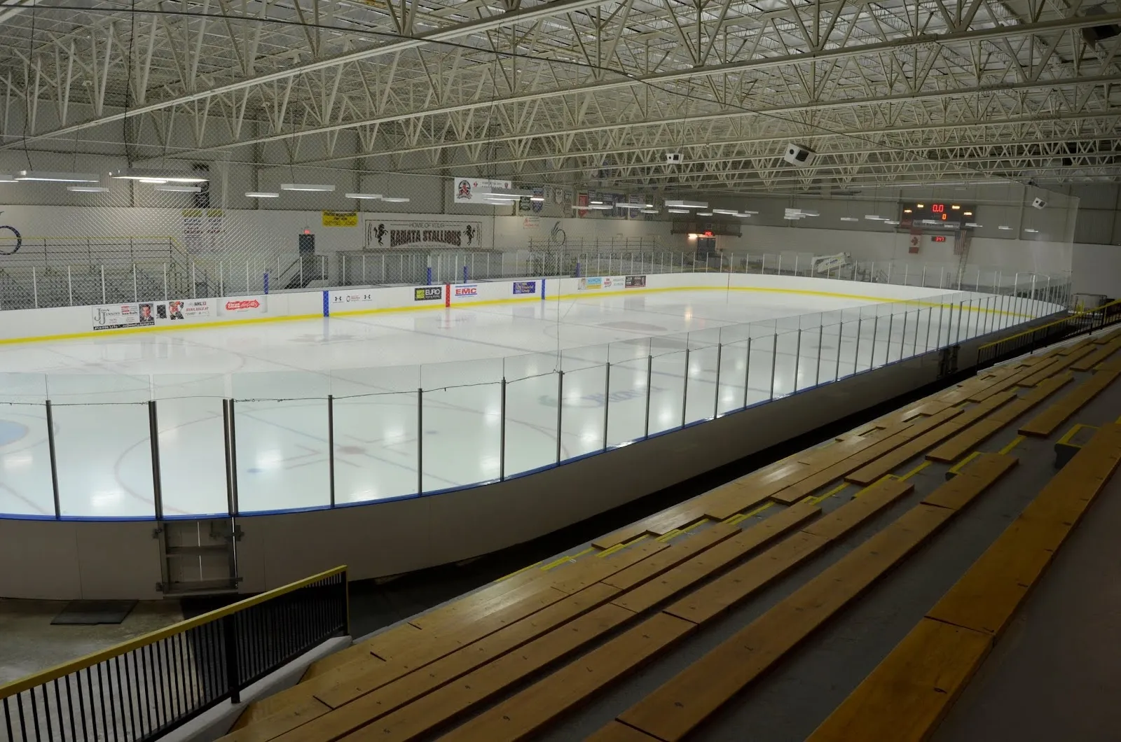 A wide view along the wooden bleachers beside the glass, the white sheet beneath a long steel-trussed roof. — Tony Graham Recreation Complex – Kanata