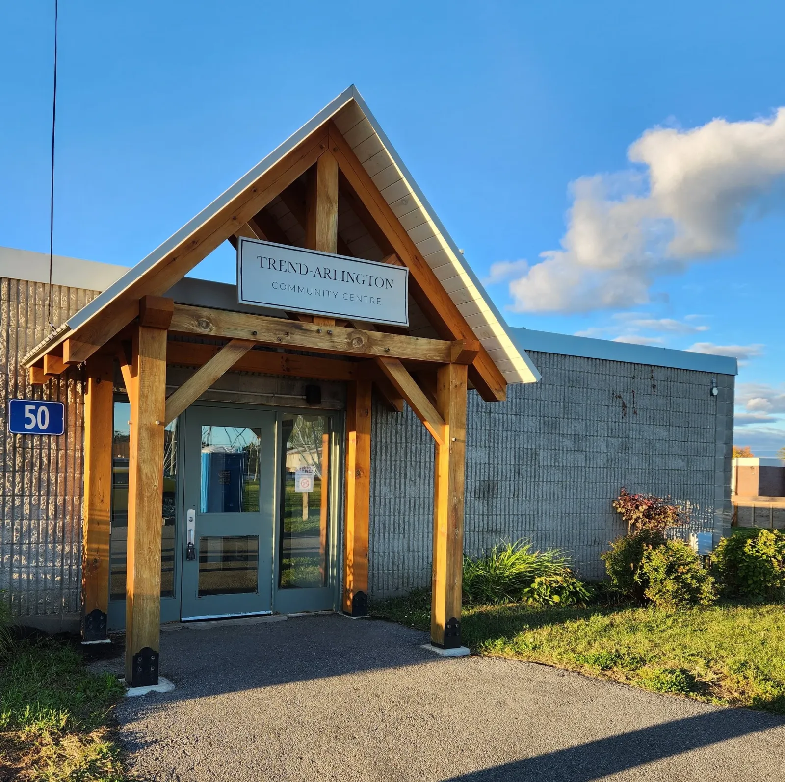 La entrada del Trend-Arlington Community Centre en 50 Bellman Drive, con su letrero de "TREND-ARLINGTON COMMUNITY CENTRE" y el número 50 del edificio, vista desde el andador del frente. — Trend-Arlington Park Outdoor Rink