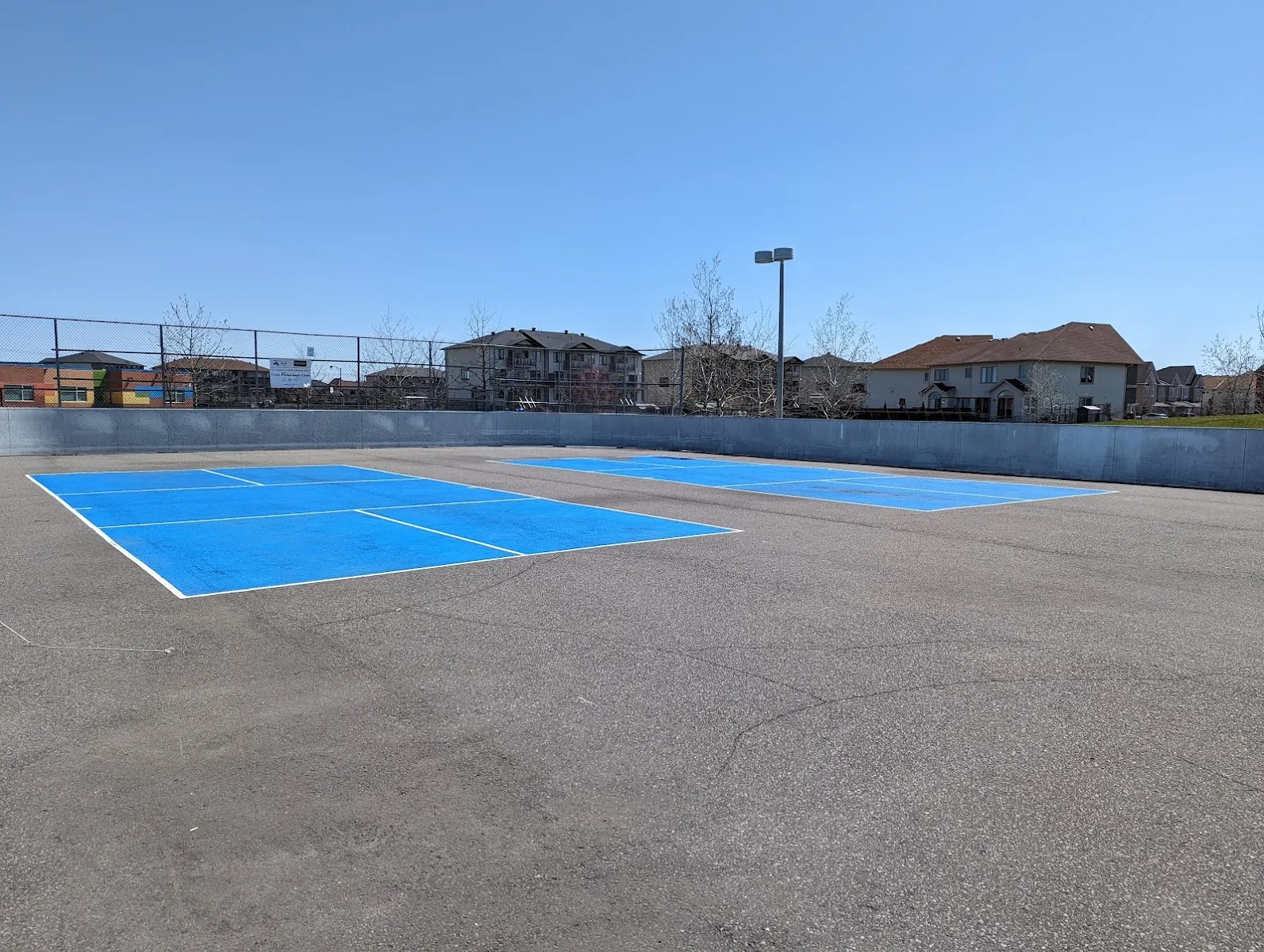 Vista Park's boarded rink pad in summer, a blue sport court inside low boards with houses beyond. — Vista Park Outdoor Rink
