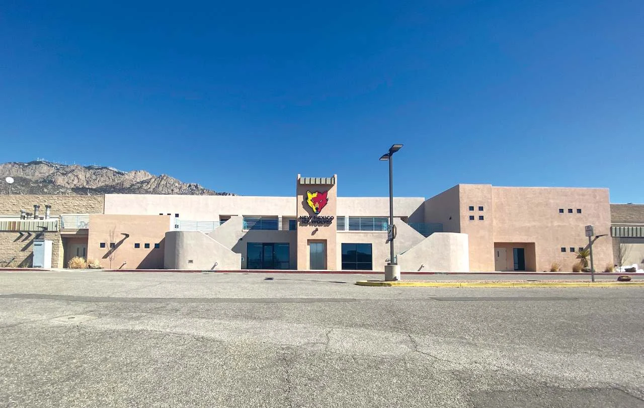 La entrada de estuco de Outpost con el logotipo de los New Mexico Ice Wolves, con las montañas Sandia de fondo bajo un cielo despejado. — Outpost Ice Arenas