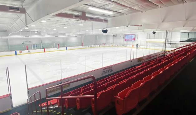 Una de las pistas vacías de Outpost vista por encima de filas de asientos rojos para espectadores. — Outpost Ice Arenas