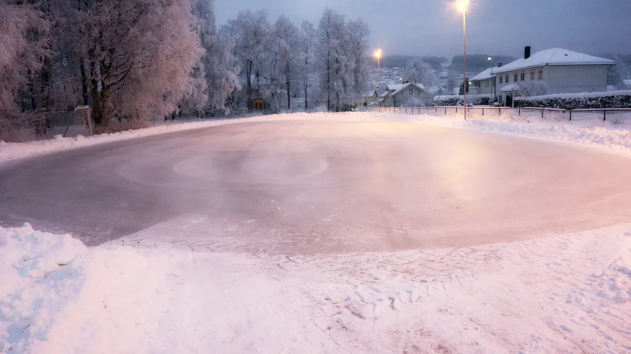 The smooth ice surface at Øyeren plass at dusk, lit pink by the sky and street lights, with frosted trees and houses behind. — Øyeren plass skøytebane (Lillestrøm)