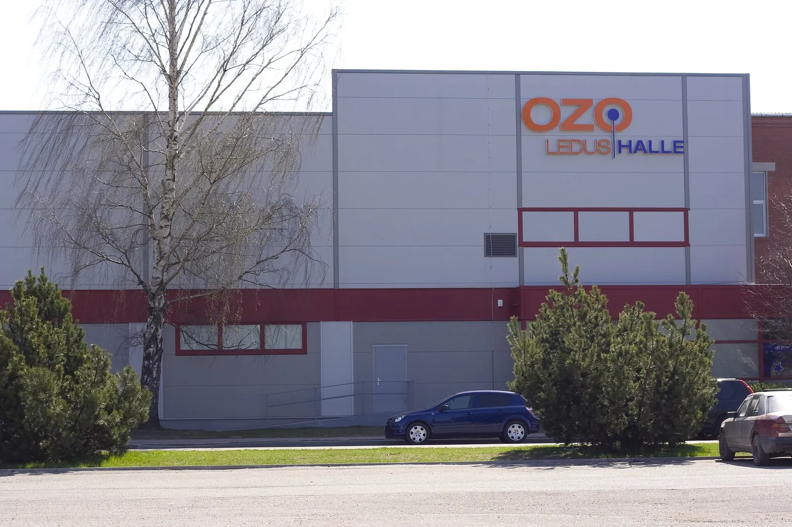 The OZO ice hall in Ozolnieki, a grey building with a red band and the OZO Ledus halle sign above the entrance. — OZO Halle