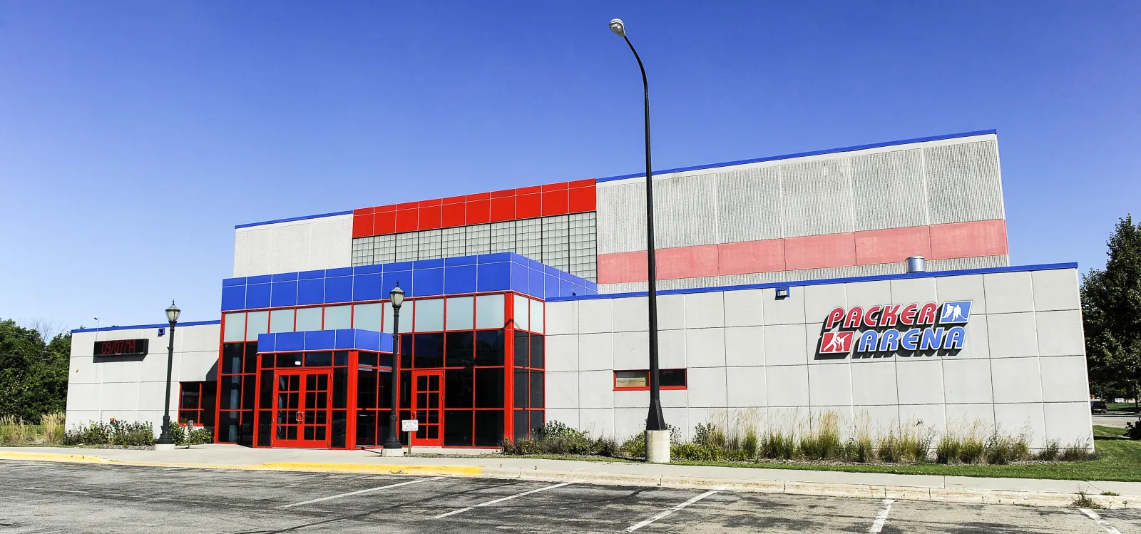 El bloque de entrada de Packer Arena con puertas de vidrio de marco rojo y un letrero de Packer Arena en el muro gris. — Packer Arena