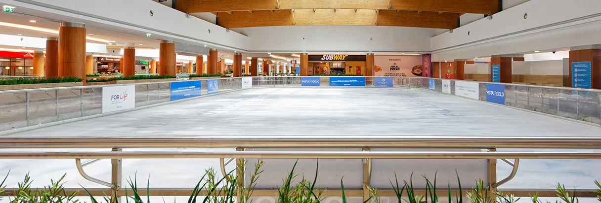 The empty ice of the Pista de Gelo inside the Palácio do Gelo Shopping, with the centre's shop fronts behind the barrier — Pista de Gelo, Palácio do Gelo Shopping