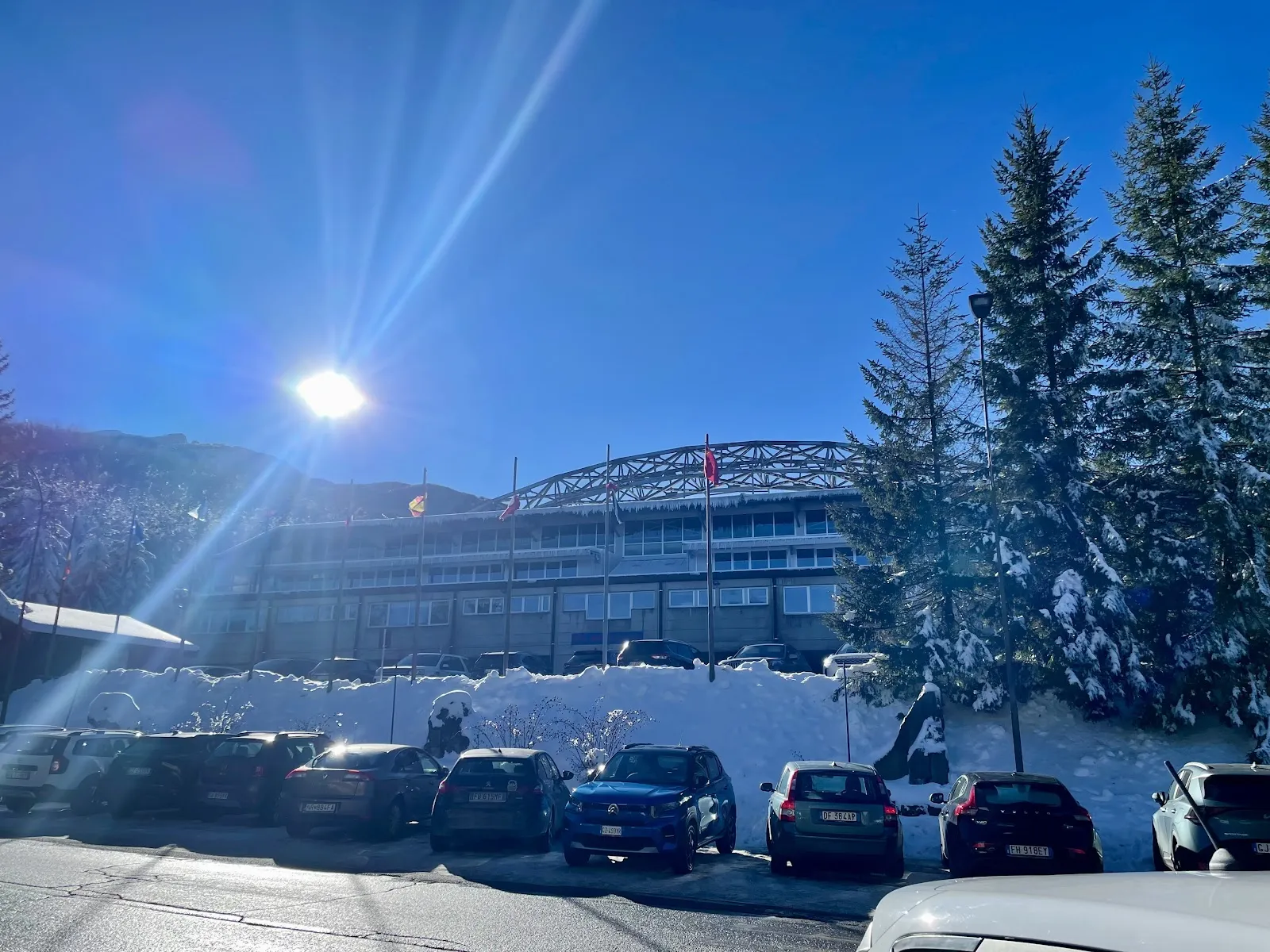 The palaghiaccio building behind the snow-covered car park, with its arched roof frame. — Palaghiaccio Cerreto Laghi
