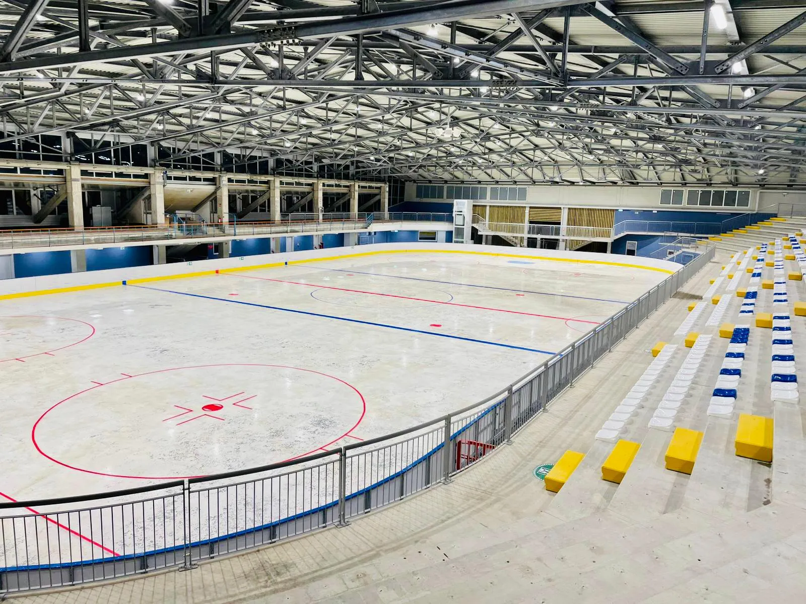The empty ice sheet with its hockey markings, boards and the stand, under the steel roof trusses after the renovation. — Palaghiaccio Cerreto Laghi