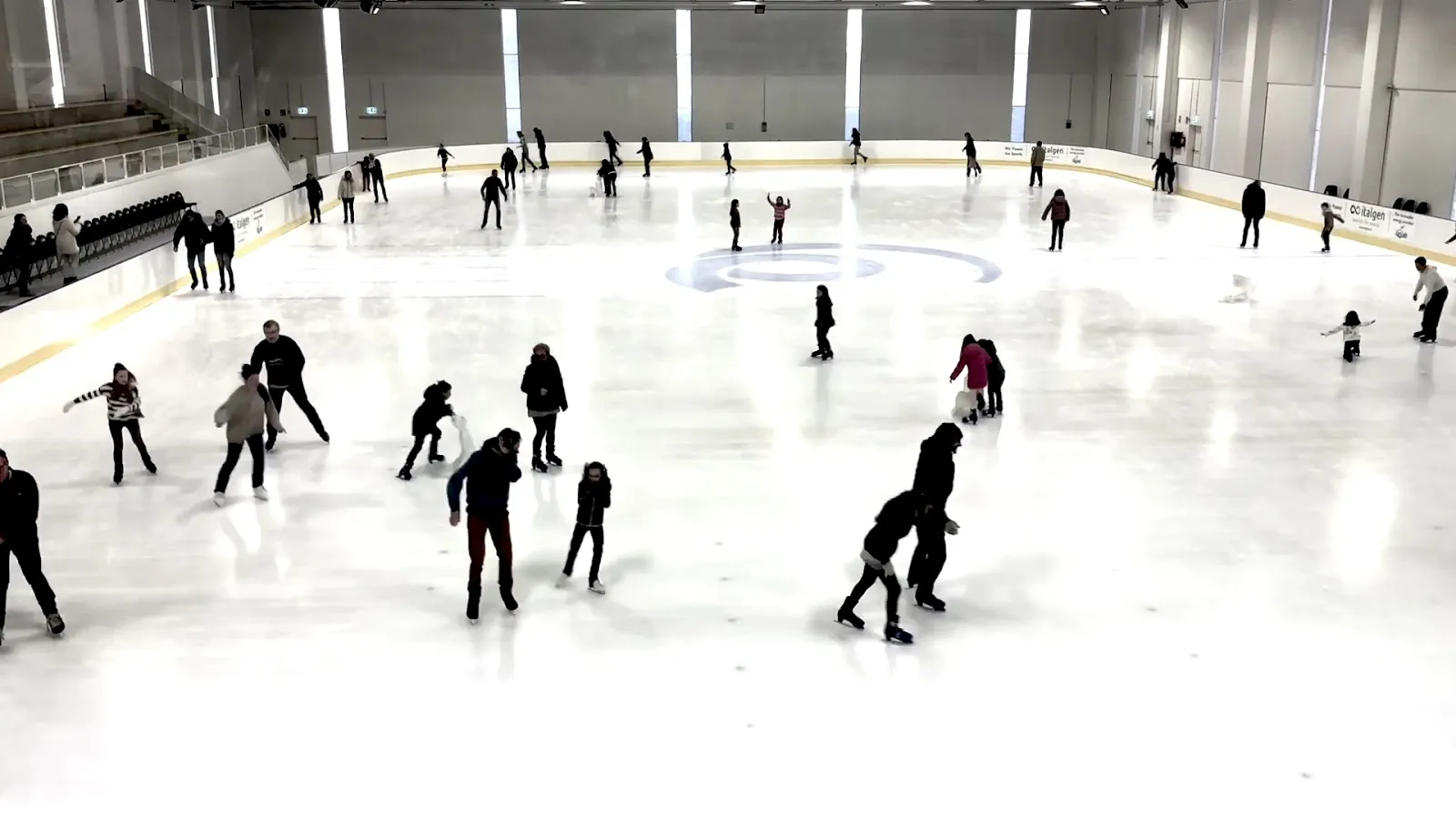 A public skating session on the large white IceLab ice sheet under the pale ceiling lights, with skaters spread across the rink. — PalaGhiaccio IceLab Bergamo
