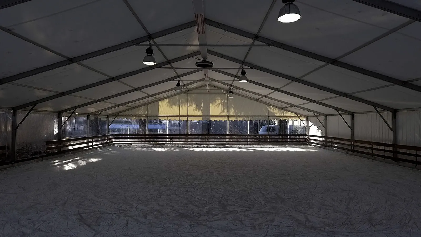 The empty ice surface inside the white tent hall, with the roof frame, lamps and the boards around the rink. — Palaghiaccio PalaExbo Saronno