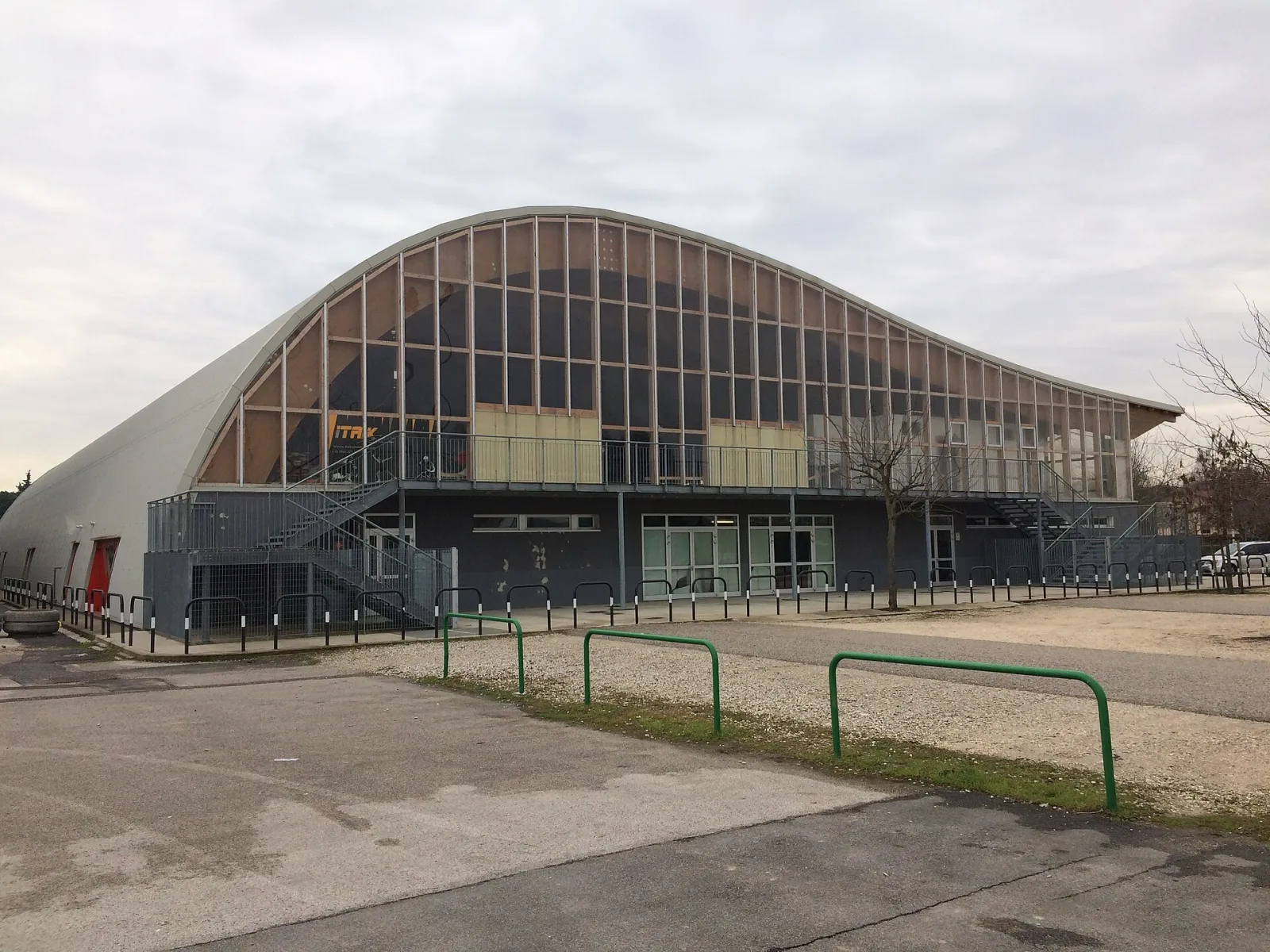 The arched timber-and-glass front of the ice hall at the Plebiscito sports centre in Padua, seen from the car park, with the stairs to the upper gallery. — Palaghiaccio Plebiscito Padova