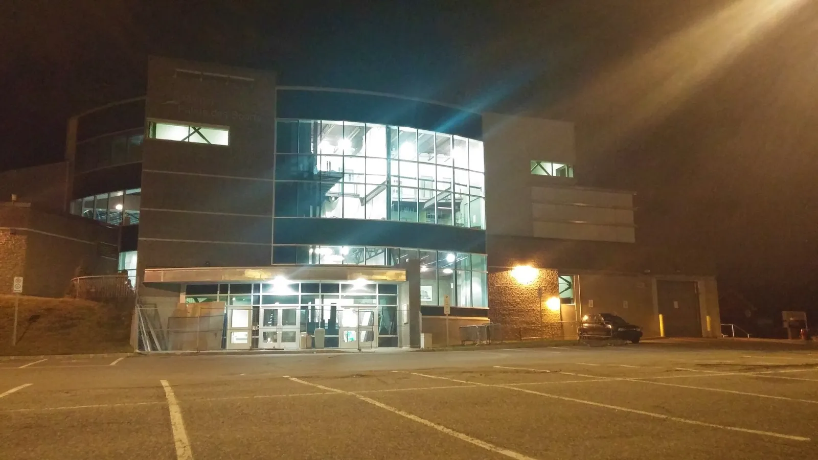 The glass-fronted entrance of the Palais des sports in Jonquière, Saguenay, seen from the parking lot at night. — Palais des sports (Jonquière)