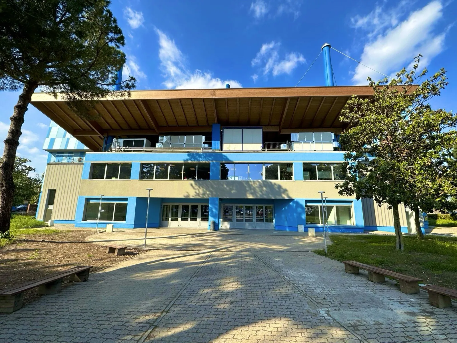 The front of the PalaSesto ice palace in Sesto San Giovanni, a blue and cream building under a wide timber roof, seen from the paved forecourt. — PalaSesto