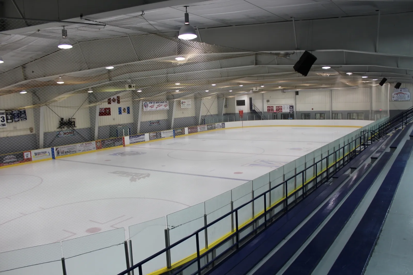 The empty ice surface of the Palmerston Arena seen from the stands, with the boards and overhead netting — Palmerston Arena