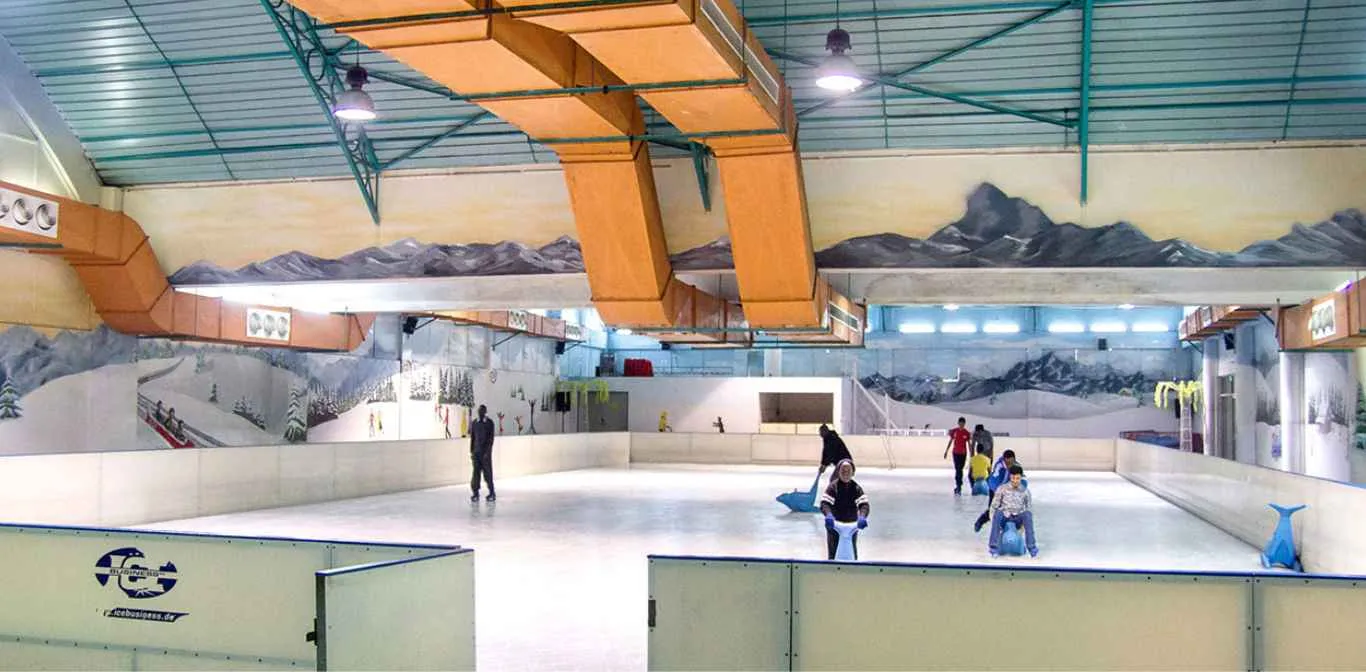The ice at the Solar Ice Rink in Nairobi seen from the boards, with a few skaters far across the sheet under the hall's roof. — Solar Ice Rink (Panari Hotel)