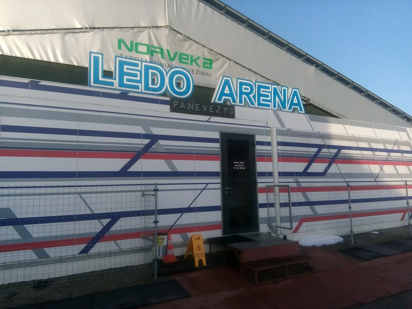 The side of Panevėžio Ledo Arena, a white tented hall with blue and red stripes and the LEDO ARENA sign — Panevėžio ledo arena