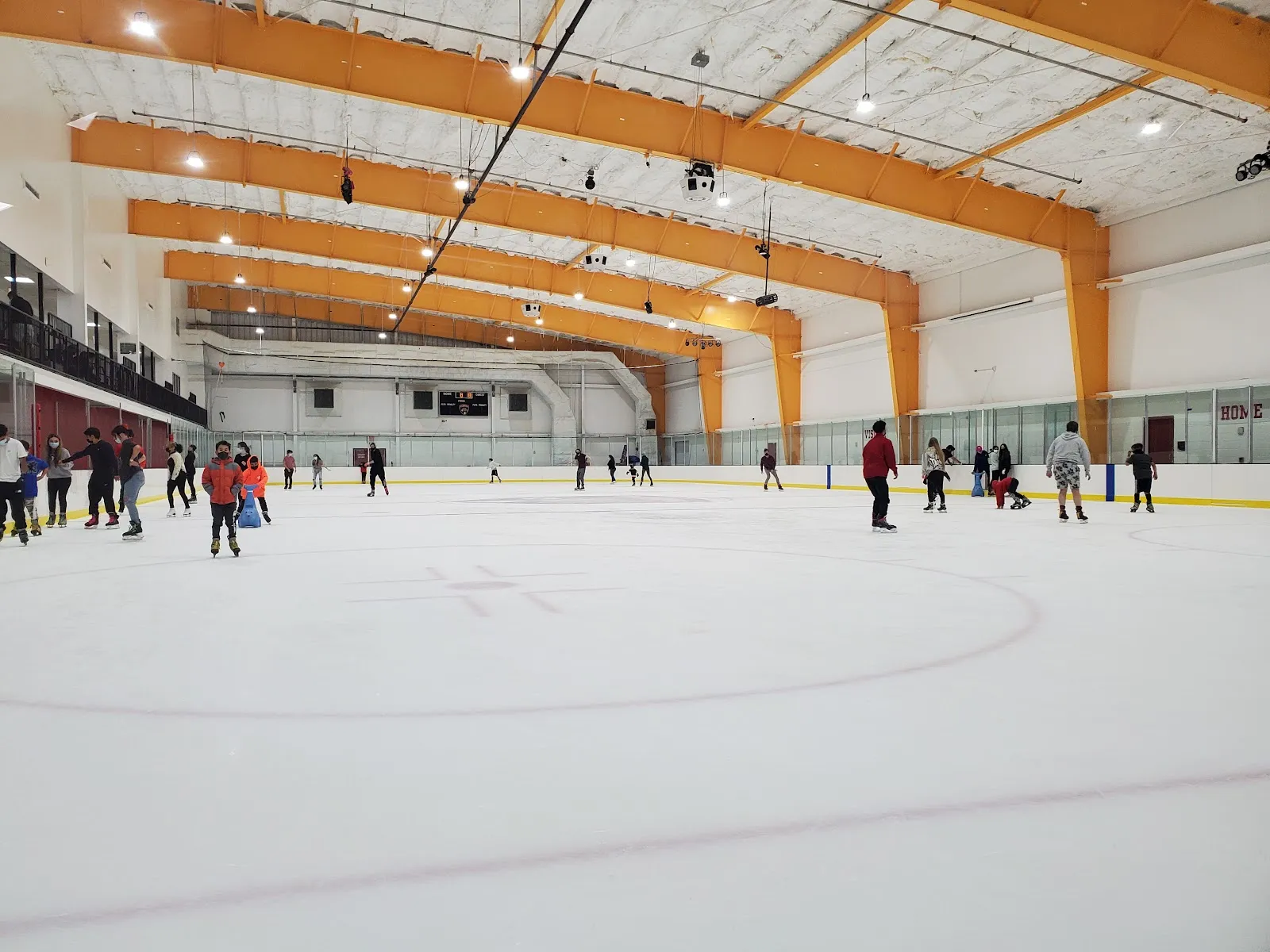 Patinadores repartidos por toda la pista durante una sesión pública, con armaduras naranjas en el techo y un marcador arriba — Florida Panthers IceDen (Coral Springs)