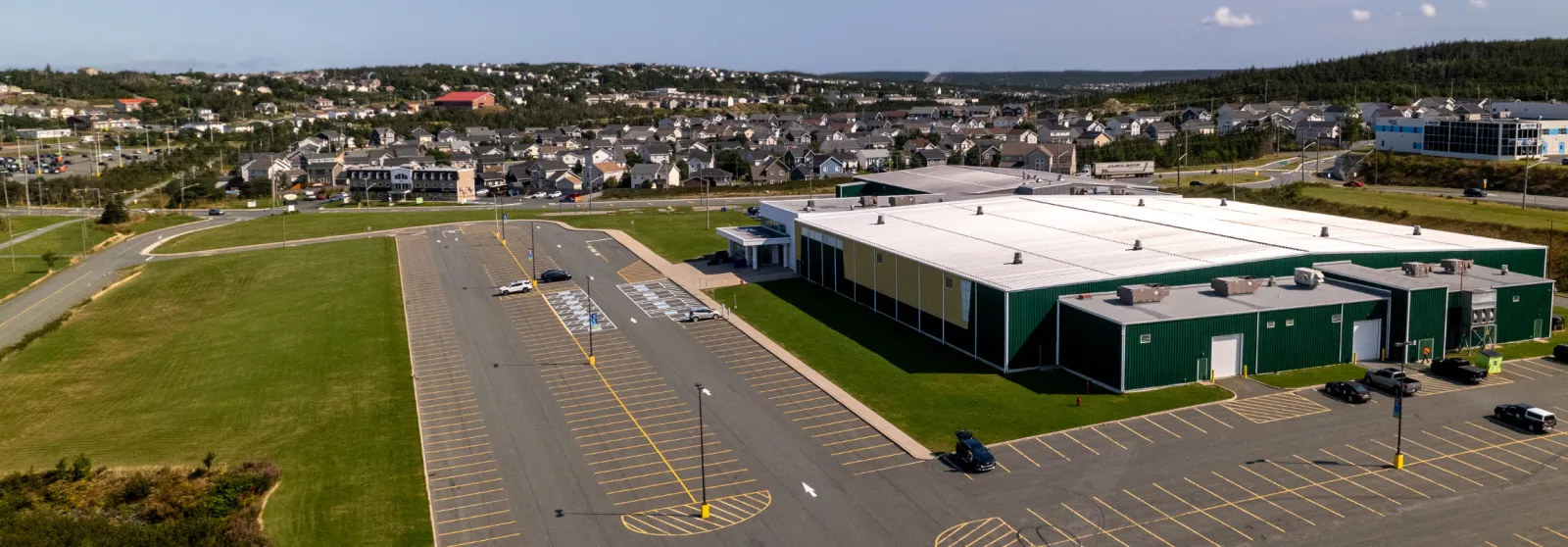 Vista aérea del edificio verde y color arena de Paradise Double Ice Complex y su estacionamiento, con el barrio de Paradise, NL, alrededor al fondo. — Paradise Double Ice Complex