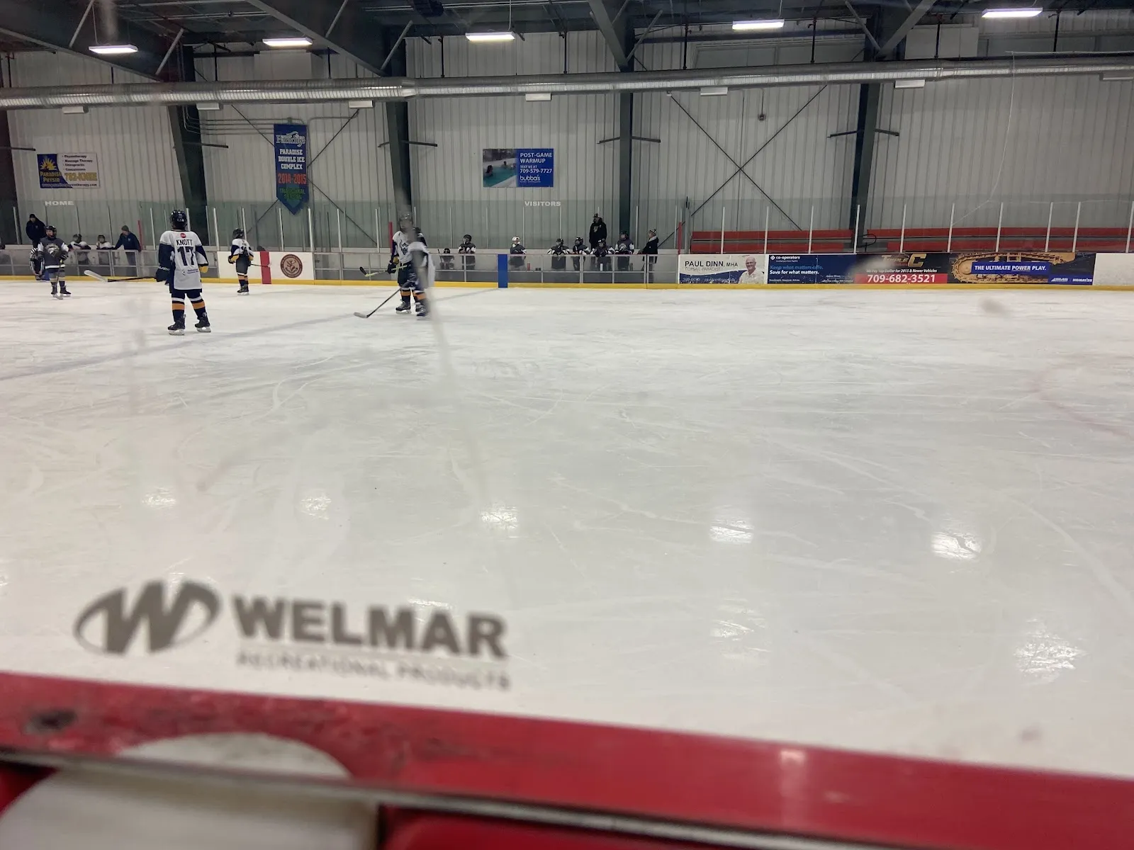 Una vista amplia de la pista desde las vallas del extremo, con jugadores repartidos por el hielo bajo un alto techo con una franja de anuncios de Gatorade en el lado cercano. — Paradise Double Ice Complex