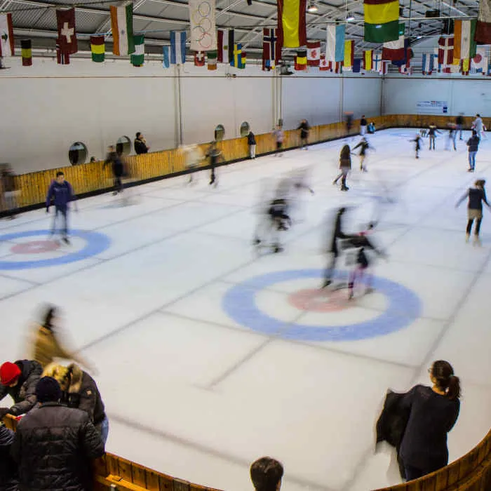 The ice rink hall of the Paradise Playcenter in Monsano, with skaters moving across the ice under rows of national flags. — Paradise Playcenter (Palaghiaccio)