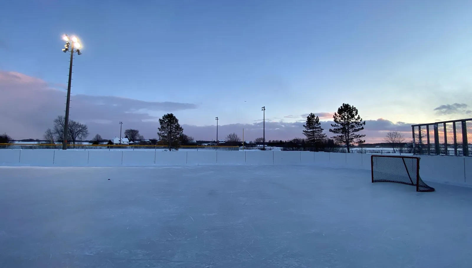 The outdoor rink at Parc de Bélair in Québec at dusk, with a hockey goal at one end, floodlights and a clear ice surface. — Parc de Bélair Outdoor Rink