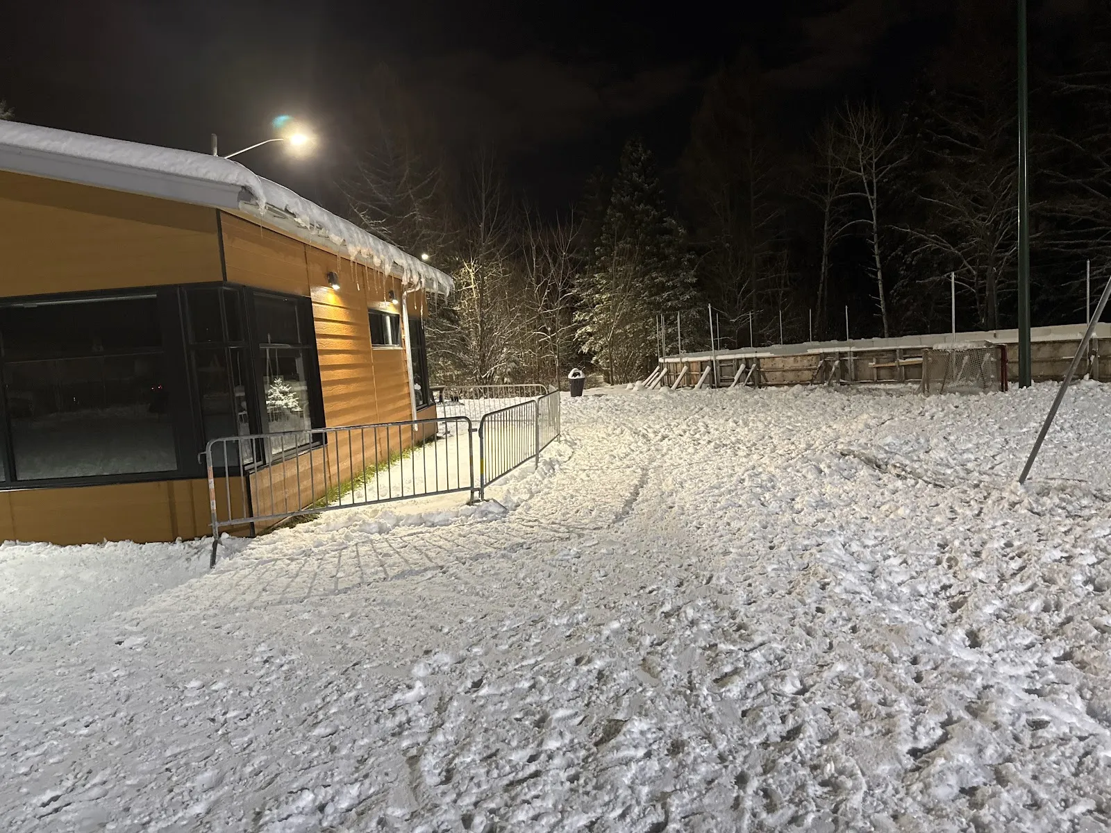 Le sentier d'hiver éclairé et le petit chalet du parc de l'Arc-en-ciel la nuit, avec de la neige au sol et les arbres du parc derrière — Parc de l'Arc-en-Ciel Outdoor Rink