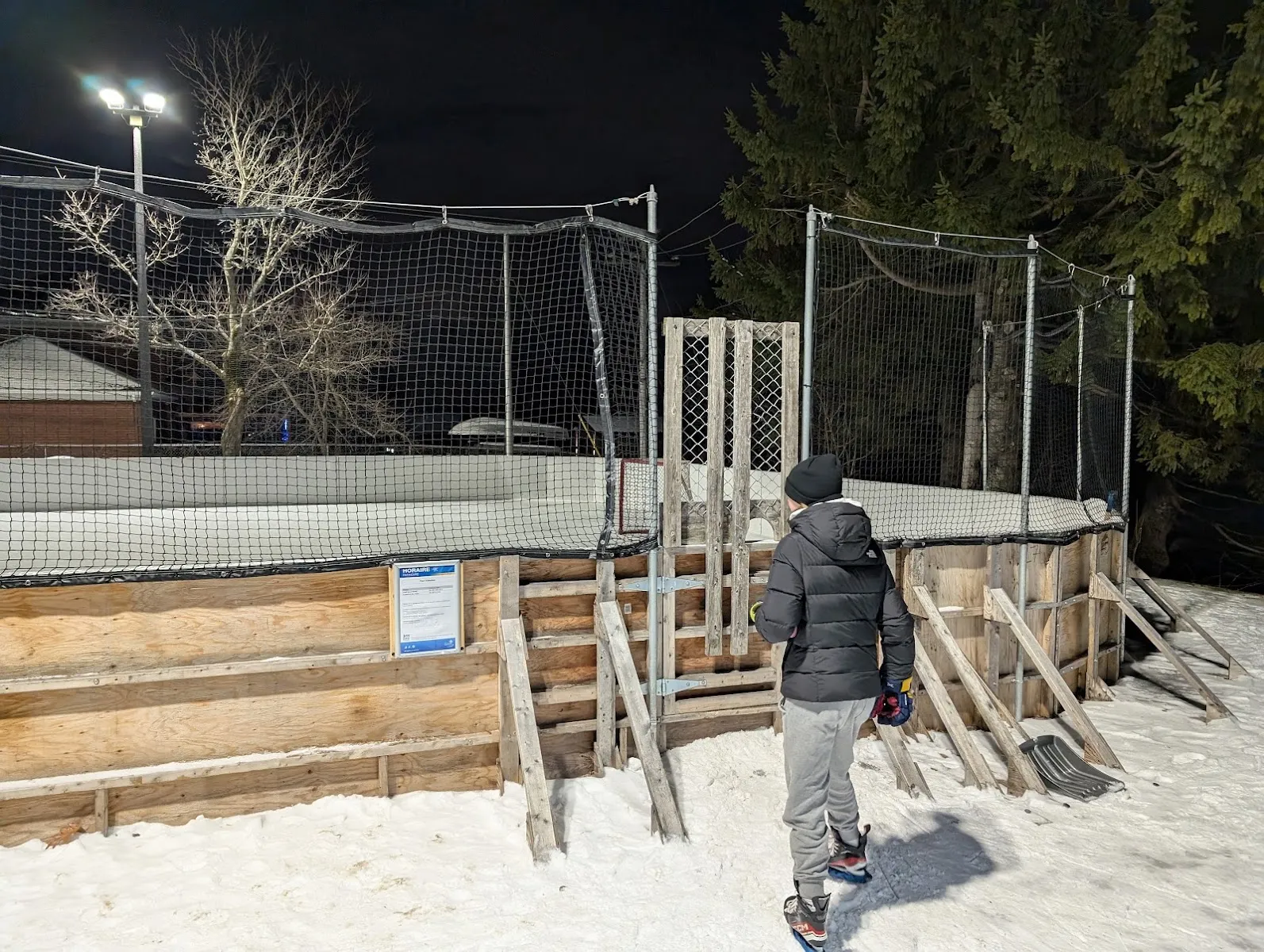 La pista al aire libre con vallas de Parc Fénelon en una noche de invierno, con vallas de madera, red y un poste de luz sobre la superficie cubierta de nieve — Parc Fénelon Outdoor Rink