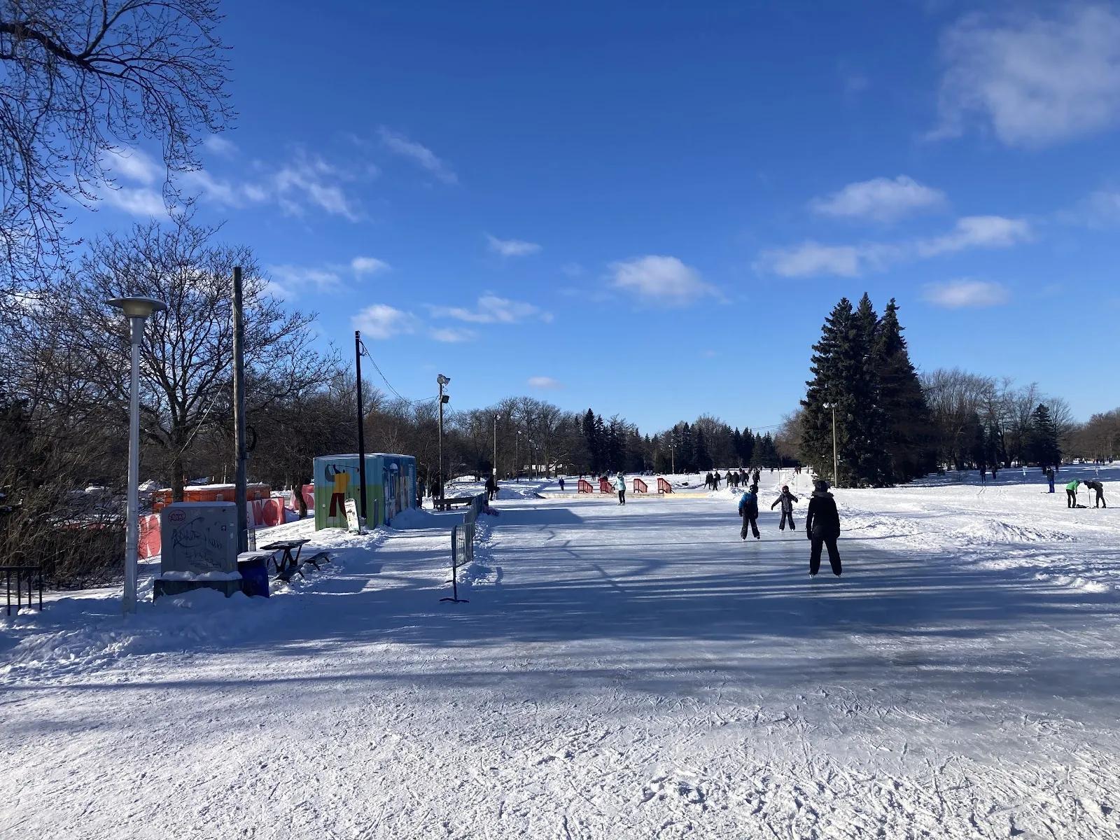 The skating area of Parc Maisonneuve in winter, an open snowy ice surface with skaters, rental huts and lamp posts — Parc Maisonneuve Outdoor Rink