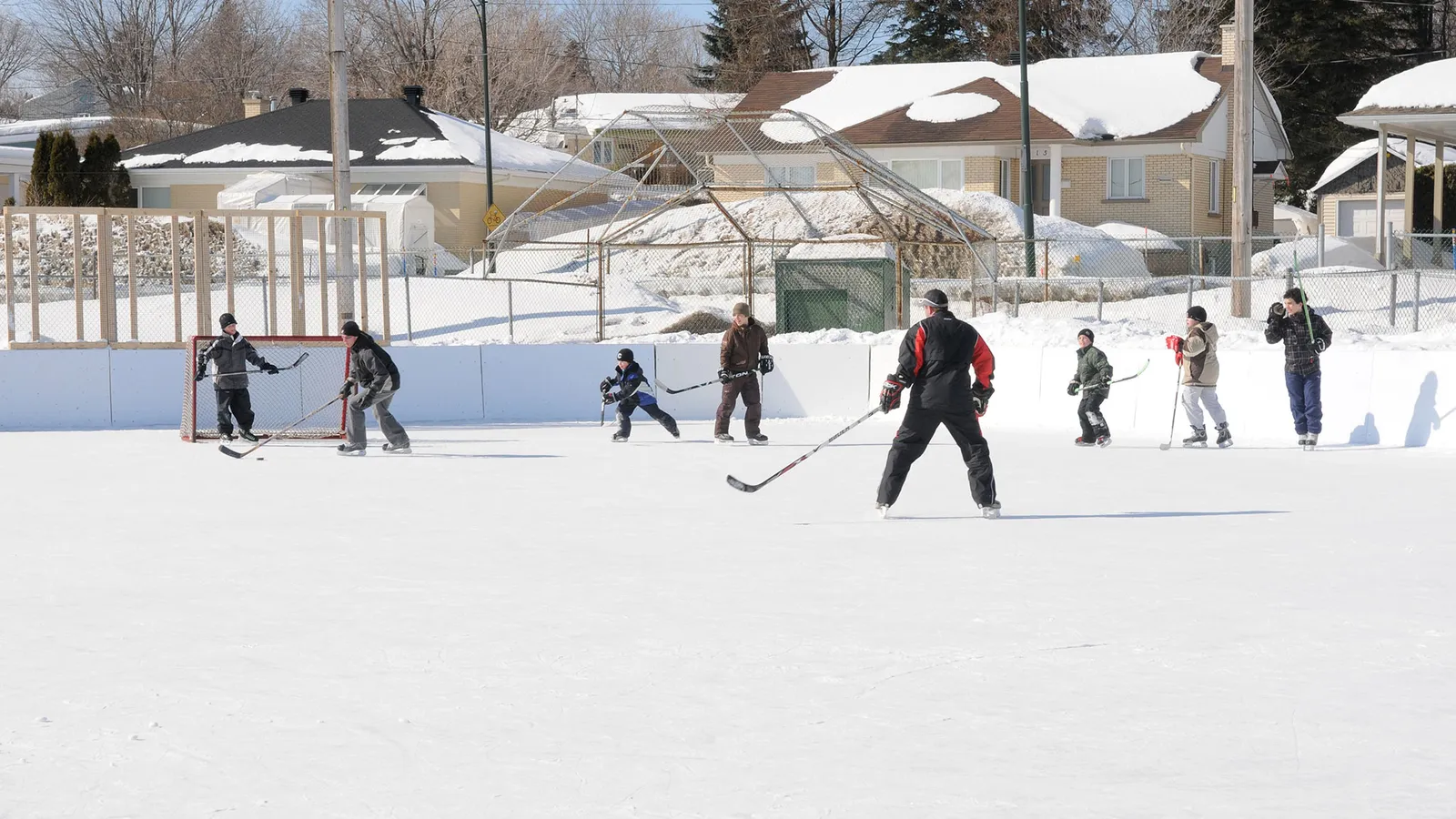 Players on the Parc Maria-Goretti outdoor rink in Québec, a few at a distance on the snow-banked ice. — Parc Maria-Goretti Outdoor Rink (Québec City)