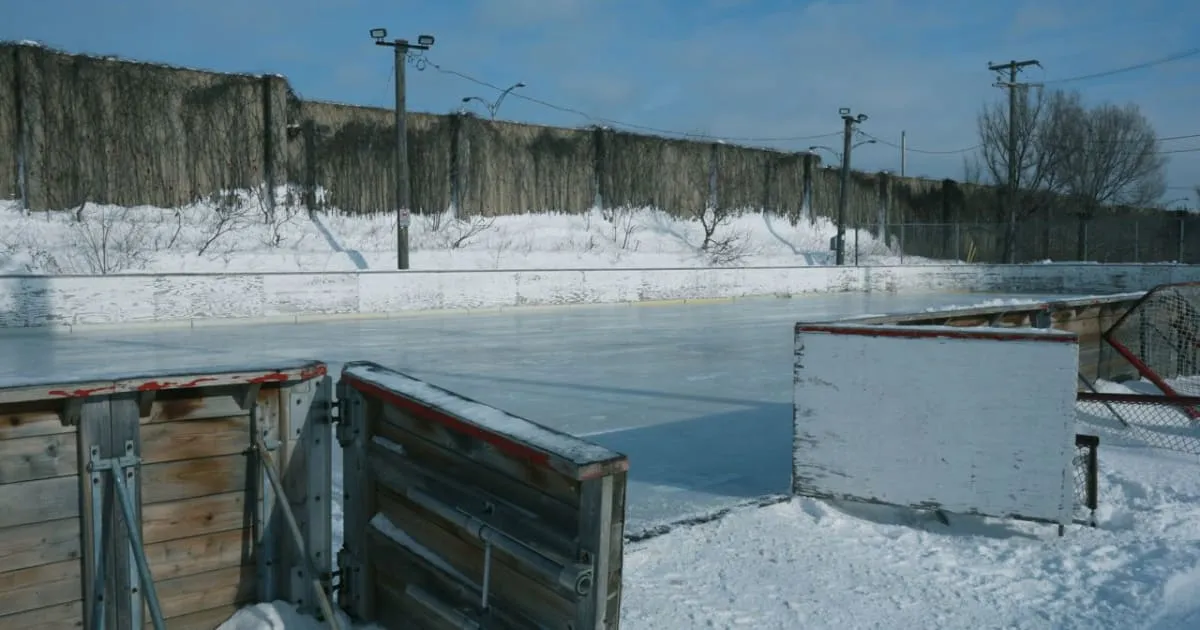 Una pista al aire libre con vallas en Parc Michel-Ménard en invierno, vallas de madera y hielo congelado con un banco de nieve junto a la puerta de entrada (foto de la Ciudad de Montréal) — Parc Michel-Ménard Outdoor Rink