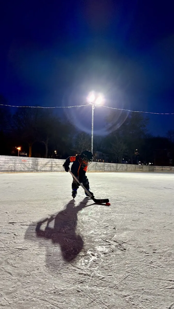 Une patinoire extérieure éclairée au parc Pierre-Bédard la nuit, les bandes et la glace sous un grand lampadaire, avec un jeune joueur en train de jouer — Parc Pierre-Bédard Outdoor Rinks