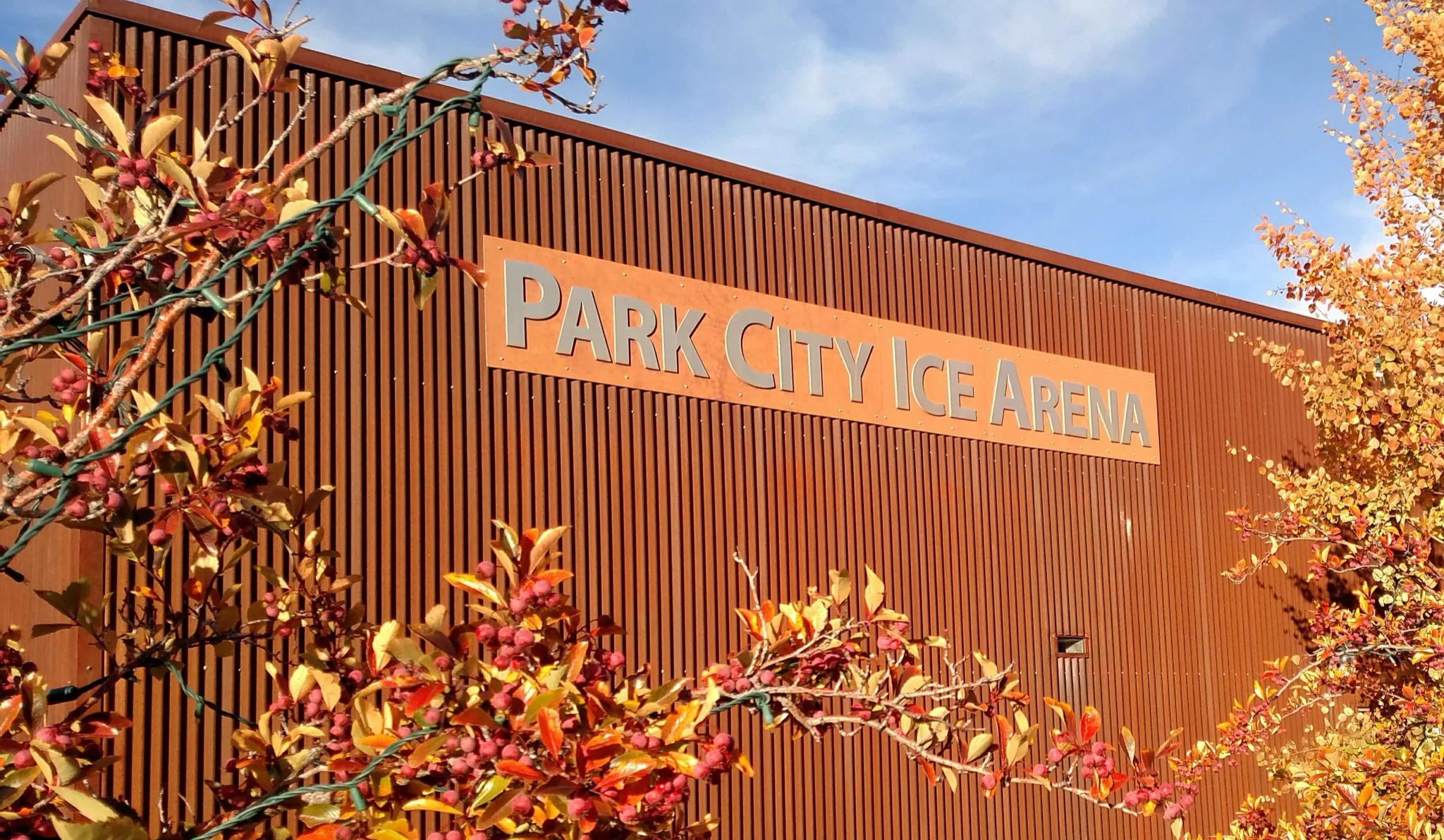Arena's rust-brown corrugated corten flank against a blue autumn sky — Park City Ice Arena