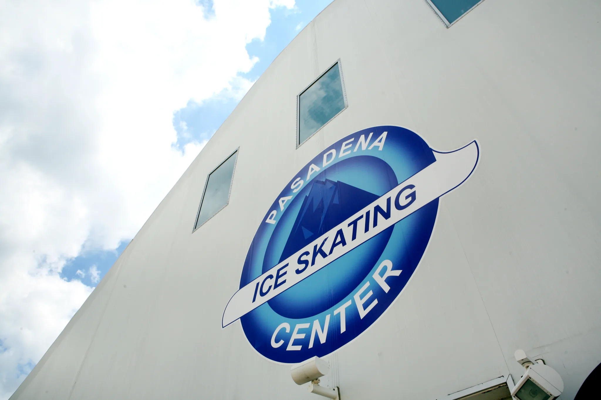Rink's white exterior wall against a blue sky with cumulus cloud — Pasadena Ice Skating Center