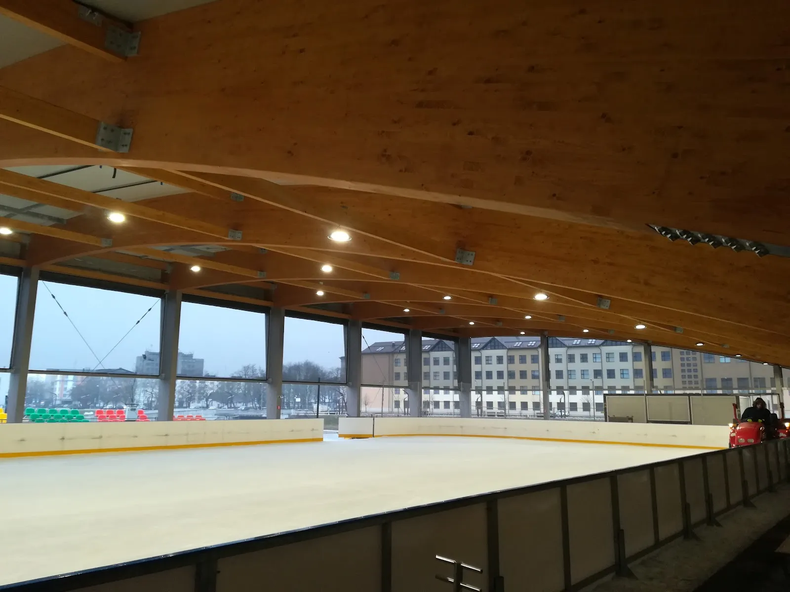 The covered ice of the Pasta sala rink in Jelgava, with the timber roof beams and the glazed side wall — Pasta salas publiskā slidotava