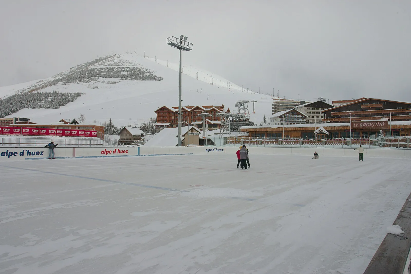 La piste de glace en plein air sous la neige, avec les pistes de ski derrière — Patinoire d'Alpe d'Huez